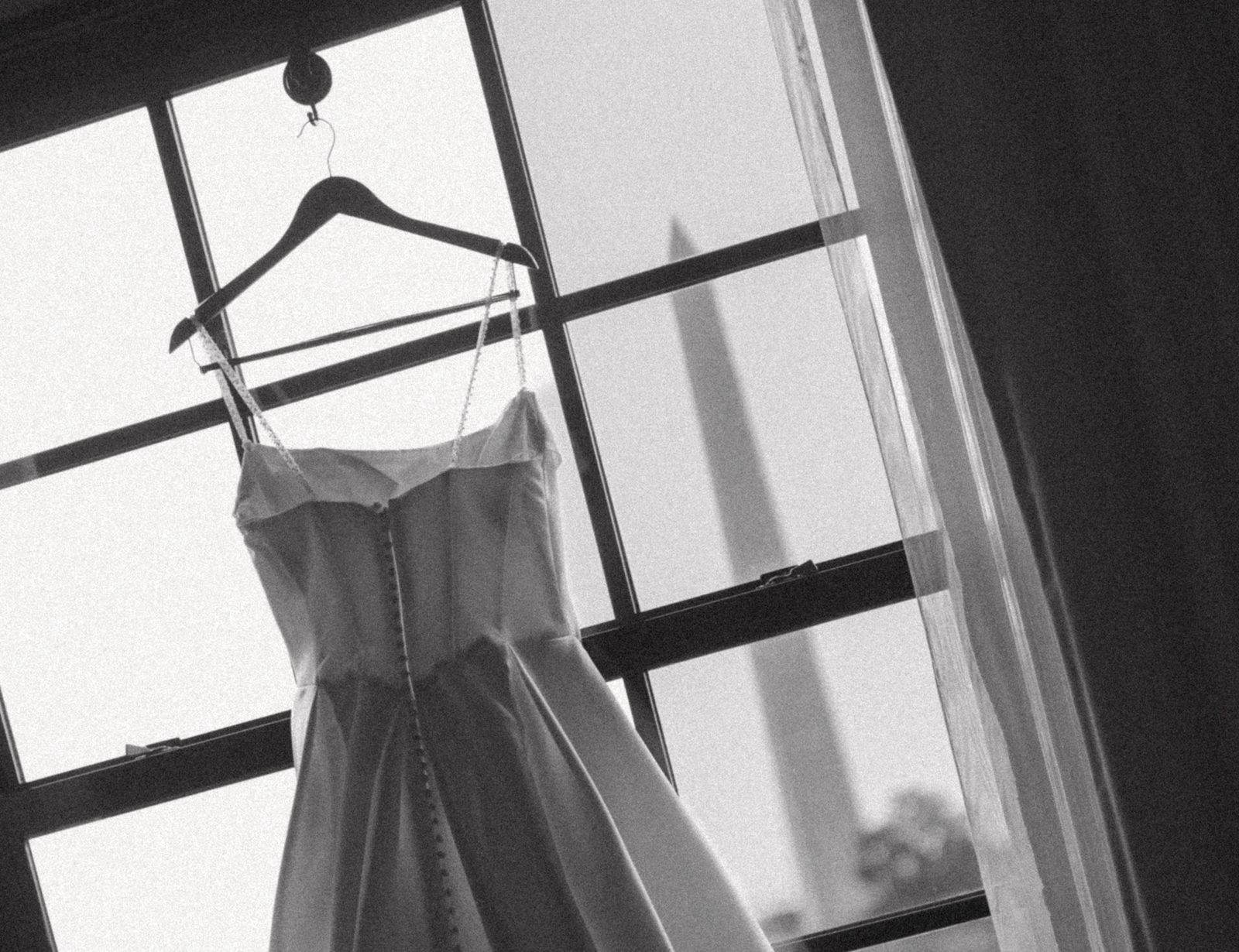 Wedding dress hanging in a window with the Washington Monument visible outside