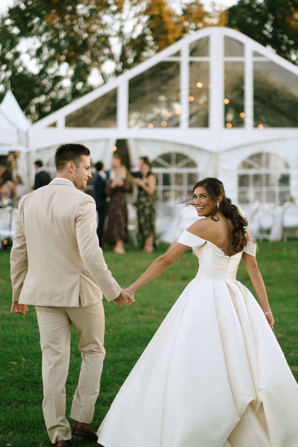 Bride and groom holding hands at tent reception